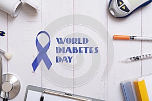 World Diabetes Day text with glucometer, stethoskope and syringes with a tablet on a wooden background, top view