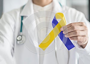 World down syndrome day blue yellow awareness ribbon on doctor`s hand for raising support on patient with down syndrome illness