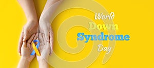 World Down syndrome day. Mom and baby are holding blue and yellow ribbon on yellow background. Down syndrome awareness concept