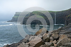 World famous Mulafossur waterfall falling from the cliff near Gasadalur village into the ocean in Faroe Islands . Misty, cloudy