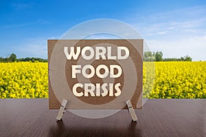 World food crisis text on card on the table with yellow field and blue sky background