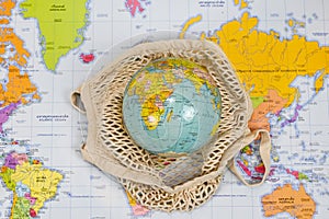 world globe in ecological mesh bag on world atlas map with thai language translation, reduce waste, plastic bag, ecological