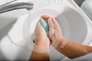 World hand washing day concept. Close-up of elderly woman washing her hands with soap in bathroom