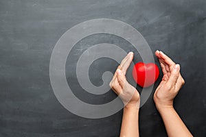 World heart day concept of young woman hand protecting red heart on black background