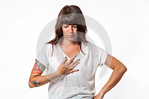 World heart day. Portrait of a young woman with a tattoo on her arm grabs her chest. White background. The concept of heart