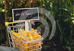 WORLD HUNGER text on Blackboard label Shopping trolley cart Filled With Pasta on agriculture background. Food and