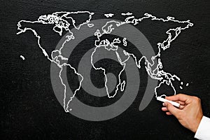 World map on blackboard. A hand draws a stylized globe map of the world with all continents.