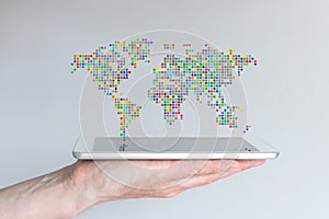 World map floating above a modern smart phone or tablet. Hand holding mobile device in front of grey background.