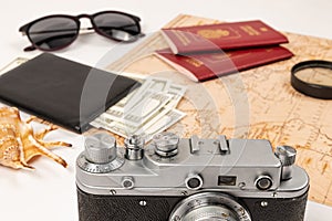 World map, two passports, a magnifying glass, money in a black leather wallet, an old film camera, sunglasses and a shell on a whi