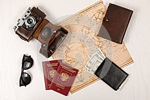 World map, two passports, money in a black wallet, an old film camera in a leather case and sunglasses on a white wooden t