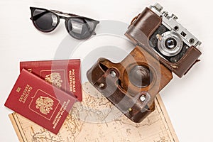 World map, two passports, an old film camera in a leather case and sunglasses on a white wooden table. view from above