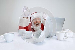 Cropped portrait of senior man wearing Santa Claus costume sitting at the desk full of empty coffee cups and looking on