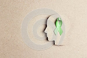 World mental health day concept. Green awareness ribbon with brain symbol on a brown background