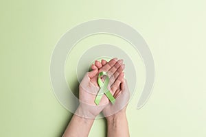 World mental health day concept. Green awareness ribbon in female hands on a green background