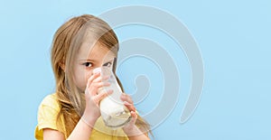 World milk day. Cute little girl drinks white milk from transparent glass on blue background. Baby child with cup of milk