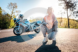 World Motorcyclist Day. A young woman with tattoos on her arm, wearing leather jacket, and posing sitting. Road and