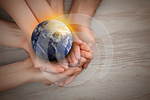 World in our hands. Top view of parents and kid holding digital model of Earth on wooden background, space for text