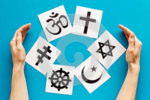 World religions concept. Hands hugs Christianity, Catholicism, Buddhism, Judaism, Islam symbols on blue background top