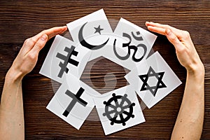 World religions concept. Hands hugs Christianity, Catholicism, Buddhism, Judaism, Islam symbols on wooden background top photo