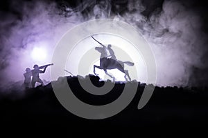 World war officer (or warrior) rider on horse with a sword ready to fight and soldiers on a dark foggy toned background. Battle sc