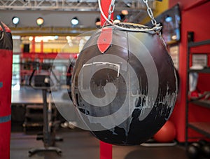 Worn, black leather wrecking ball style heavy bag hanging at a boxing gym