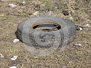 A worn car tire is wallowing in mud and a puddle on the ground. Environmental pollution. Ecological problems