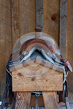 Worn comfortable leather western saddle on a wood saddle stand against a rustic wood wall