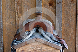 Worn comfortable leather western saddle on a wood saddle stand against a rustic wood wall