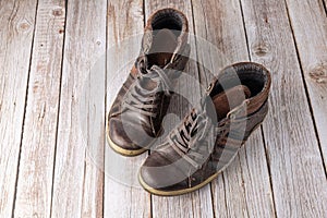 Worn old pair male leather shoes on wooden floor. Brown dirty used male boots