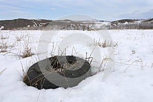 A worn-out car tire lies in a field in winter in the snow. Landfill of used tires and automobile waste. Recycling of automobile