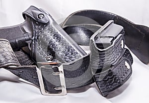 A worn police duty belt with a black pistol and two pistol magazine case wrapped up