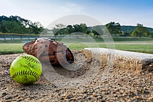 Worn softball and glove on pitcher`s mound in early morning