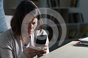 Worried adult woman reading news on phone at night at home photo