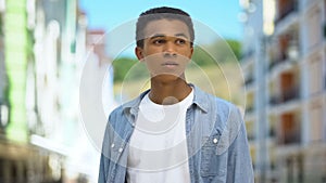 Worried Afro-American teen boy standing outdoors, waiting for friends late