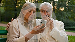 Worried aged 70s Caucasian family retired couple senior man woman using mobile phone device scrolling internet website