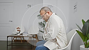 Worried, attractive middle-aged caucasian man suffering serious stomachache while sitting uneasily on a chair in a medically