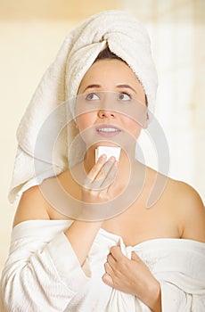 Worried beautiful young woman with a white towel covering her head is cleaning her chin with a small piece of paper in