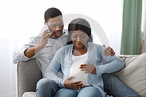 Worried black man calling doctor while wife having labor pains