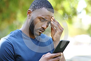 Worried black man checking smart phone in a park