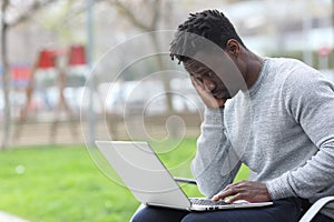 Worried black man reading bad news on laptop at the park