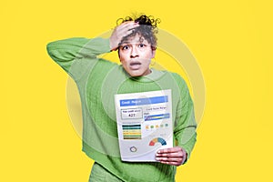 Worried black woman holding poor score credit rating isolated on yellow background