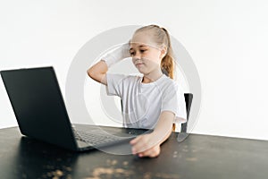 Worried blonde little girl put broken hand wrapped in white plaster bandage on head thoughtful looking to laptop screen