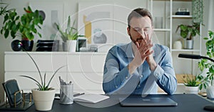 Worried businessman closing laptop sitting with hands clasped