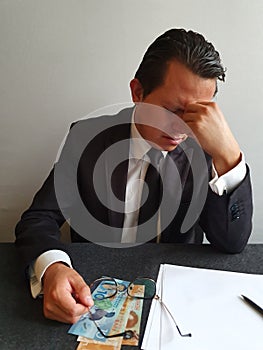 worried businessman with hand on his face and New Zealand money on the table