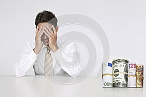 Worried businessman at table with money rolls representing financial problems