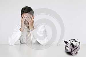 Worried businessman at table with trapped piggy bank representing financial difficulties