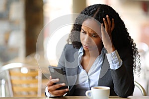 Worried businesswoman checking smart phone in a bar terrace