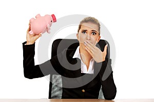 Worried businesswoman with a piggybank behind the desk