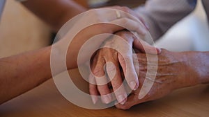 Worried caucasian man gently stroking hand of his sick old mother showing care or love. Son comforting wrinkled arm of