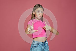 Worried child girl pointing by fingers on herself and showing amount size gesture, standing on pink studio background